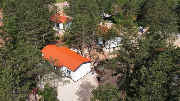 A finished house with an orange roof among the pines at the Citadel.Garden village, with further units going up behind it