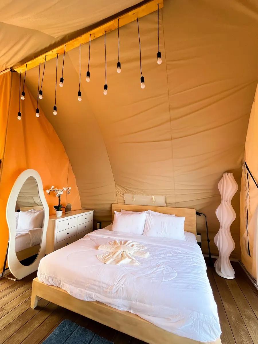Inside a glamphouse at the Reef Resort: a double bed under the peaked canvas, with a dressing table and hanging lights