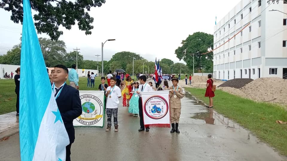 Residents marching with Honduran flags in a community parade at Ciudad Morazán
